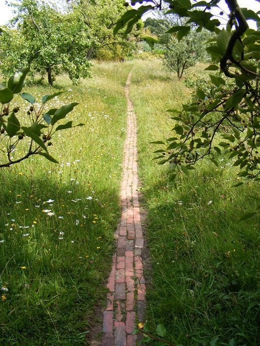 This may contain: a brick path in the middle of a grassy field
