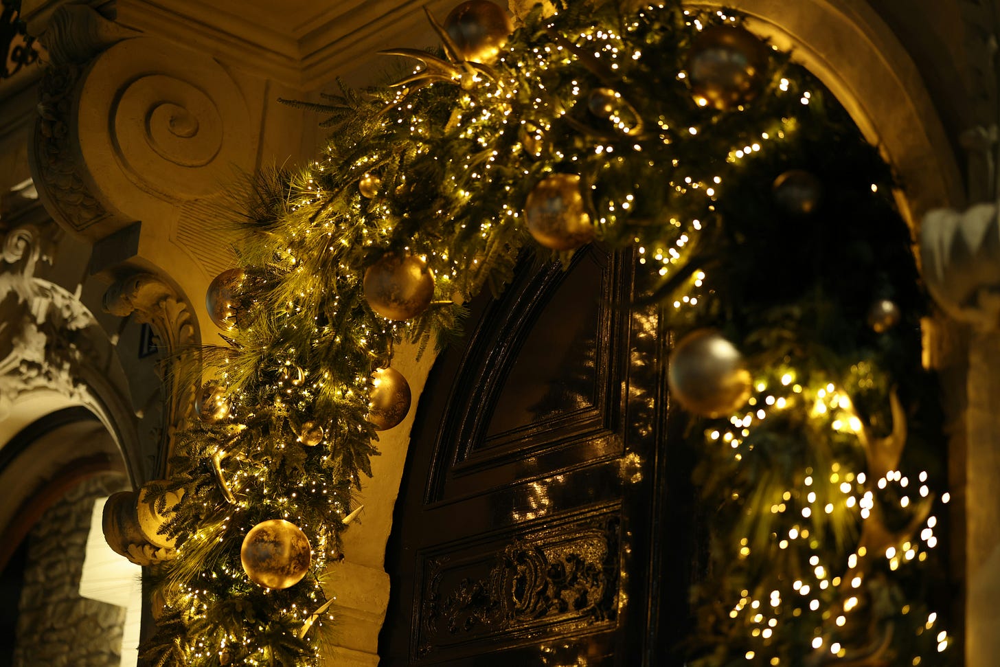 A lit christmas wreath arches over an intricately carved door. A lit christmas wreath arches over an intricately carved door.