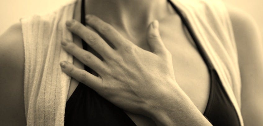 woman in white vest and black bikini with hand on chest