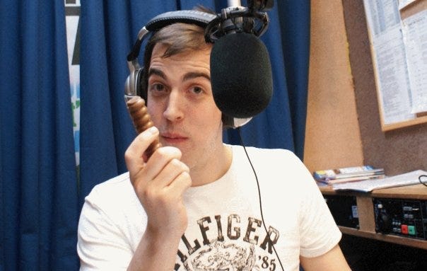 Dean is sitting behind a microphone in a radio studio holding a chocolate bar.