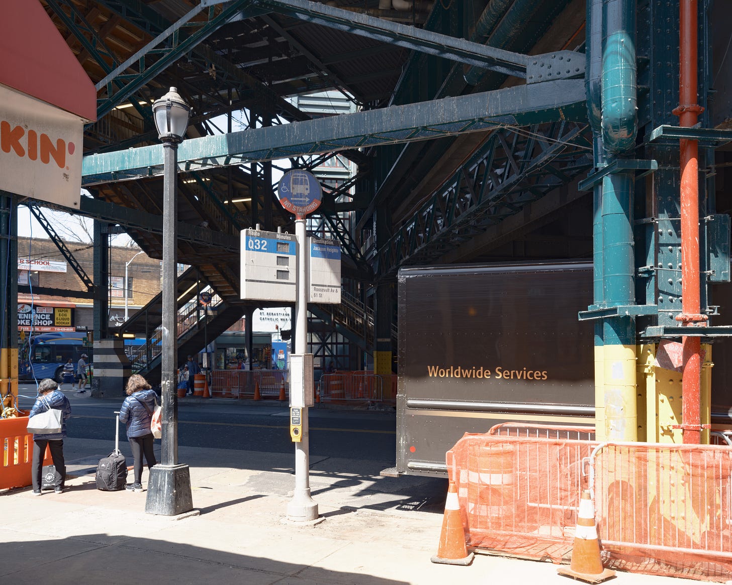 People waiting in a patch of sunlight underneath the elevated train tracks