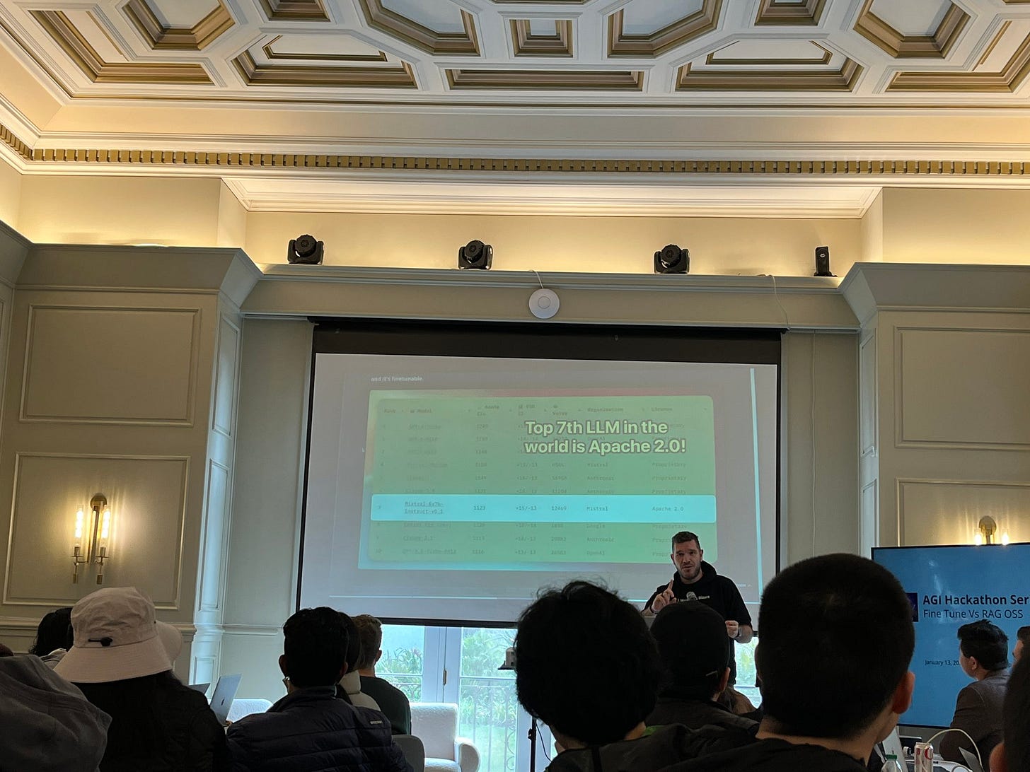 Alex at the front of the room with a slide that says top 7th LLM in the world is Apache 2.0