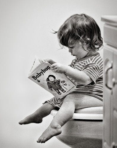 Child sitting on toilet reading a book.