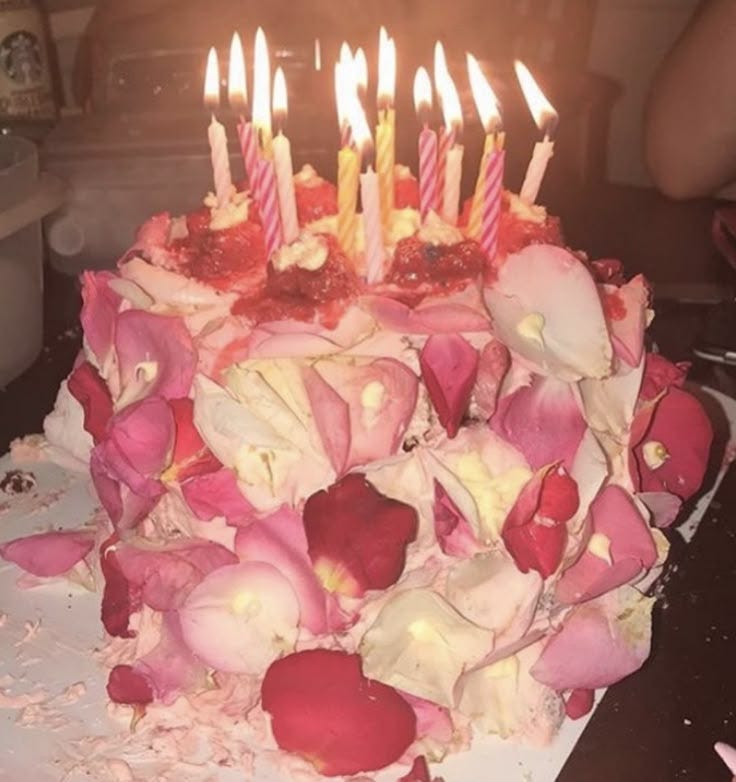 This may contain: a birthday cake with pink and white flowers on it that has lit candles in the middle