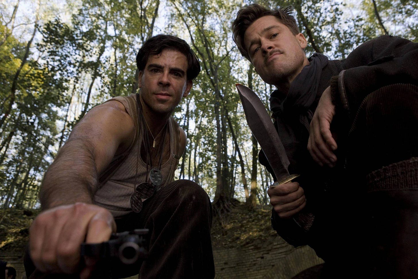 two men, one with a knife, look down with satisfaction into the camera
