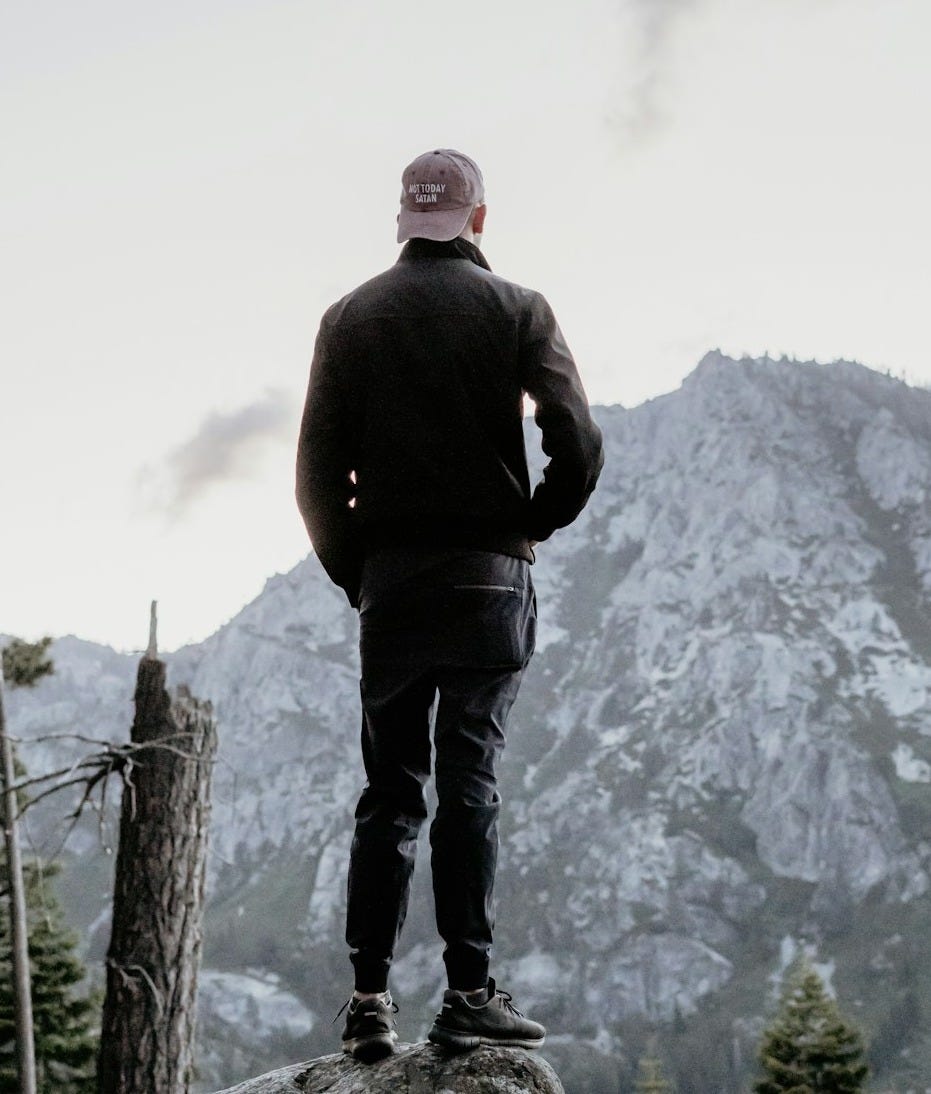 man standing on gray rock looking at mountain peak man standing on gray rock looking at mountain peak