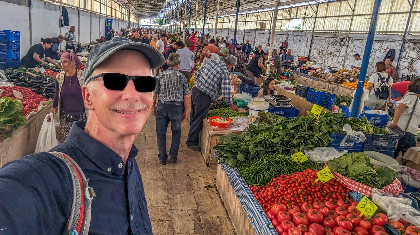 Michael inside the Fethiye weekly market, produce stalls lined up behind him. 