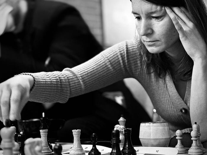 Woman with hand on forehead playing chess in black and white