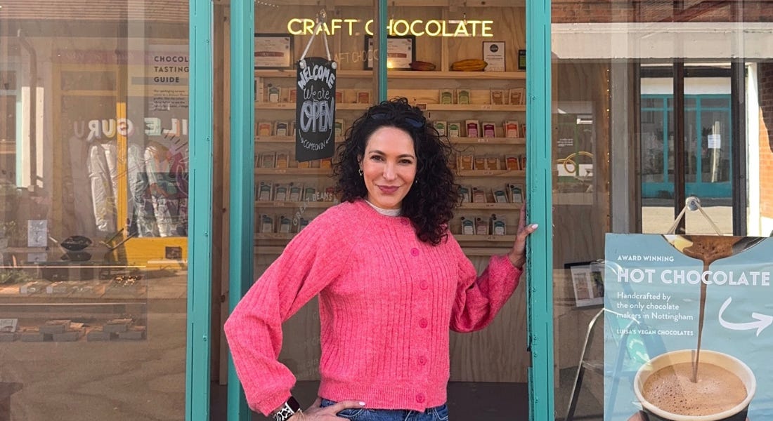 Luisa Vicinanza-Bedi wearing a pink cardigan standing in her blue shop doorway, with her shop behind her Luisa Vicinanza-Bedi wearing a pink cardigan standing in her blue shop doorway, with her shop behind her