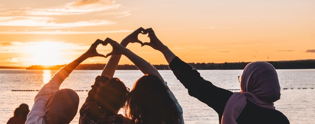 four people sitting on shore forming hearts with their hands during golden hour four people sitting on shore forming hearts with their hands during golden hour