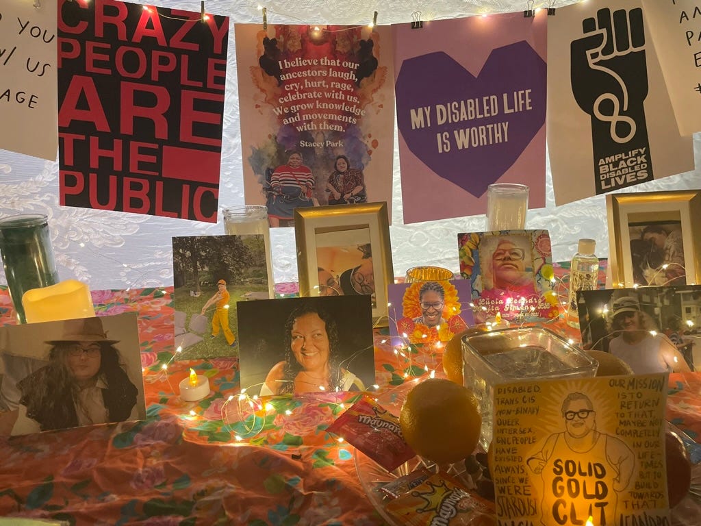image of the disabled grief portal altar, art by various artitst that says CRAZY PEOPLE ARE THE PUBLIC in red on black, My Disabled Life Is Worthy in purple heart, We Need Your Disabled age above images of ancestors on a flowers cloth scattered with fairy lights, with fruit and candy offerings