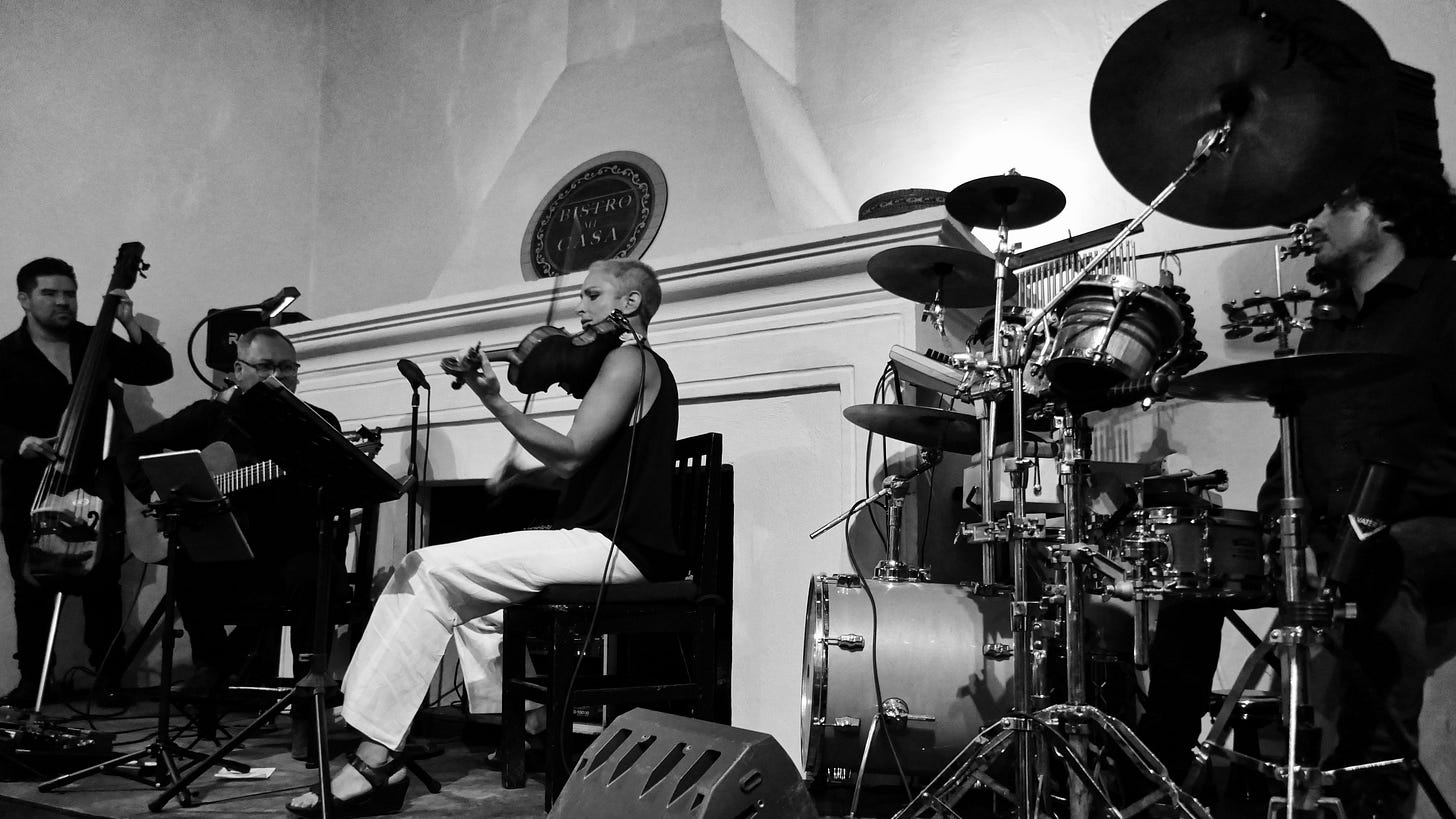 A black and white image of a live music performance, featuring musicians playing a variety of instruments in an intimate setting. A black and white image of a live music performance, featuring musicians playing a variety of instruments in an intimate setting.