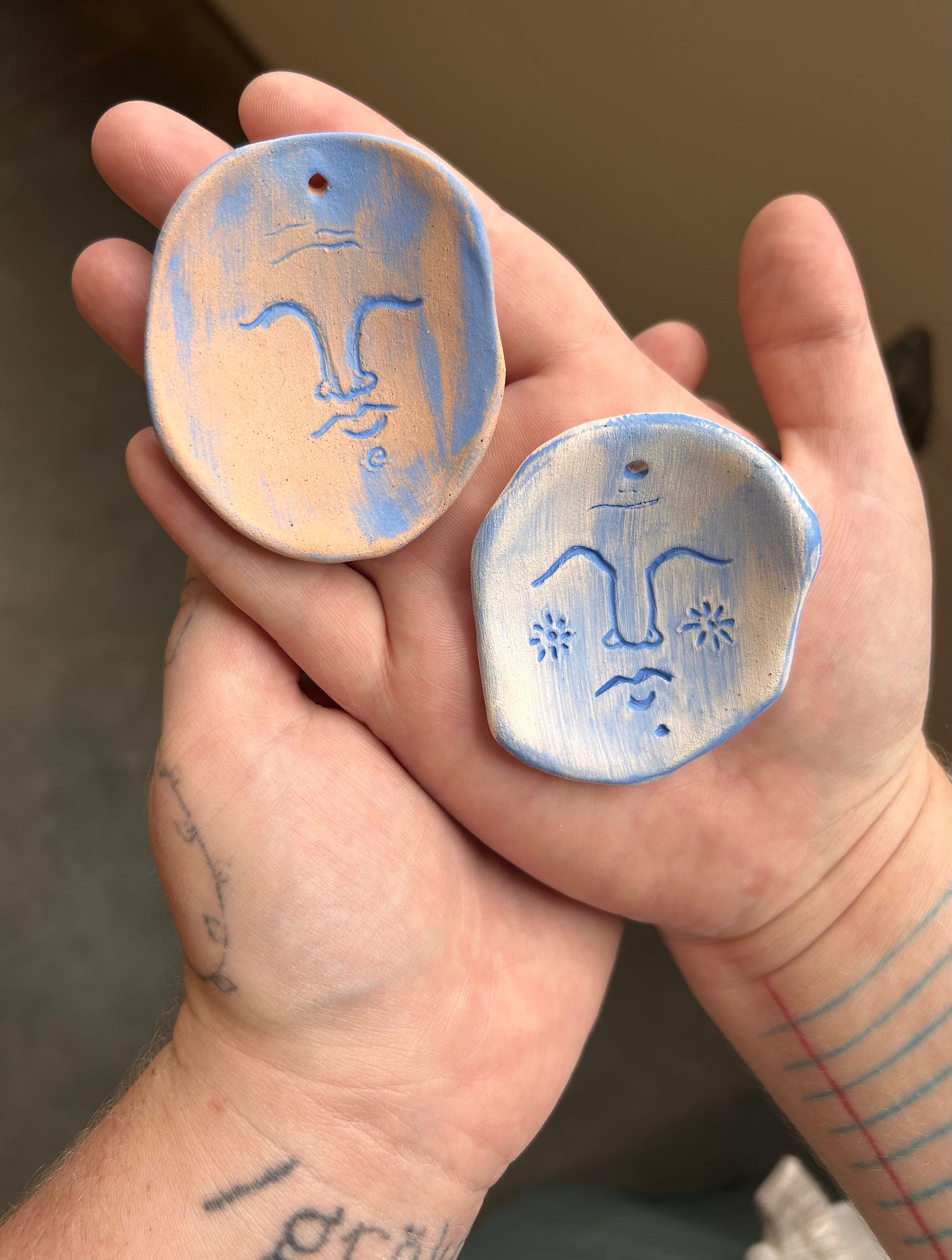 My wife's hands holding two small clay tablets painted with elegant blue faces My wife's hands holding two small clay tablets painted with elegant blue faces