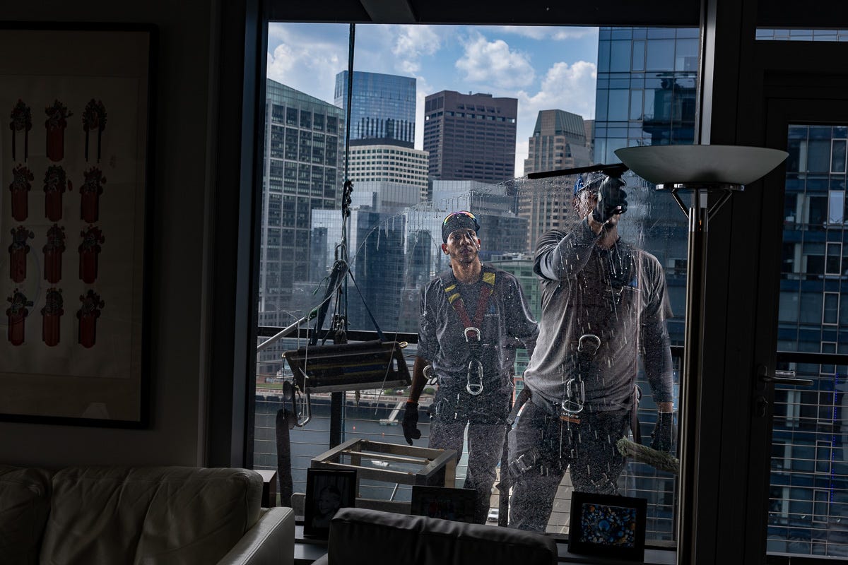 Two window washers working together to clean balcony windows while standing on the 14th-floor balcony. Two window washers working together to clean balcony windows while standing on the 14th-floor balcony.