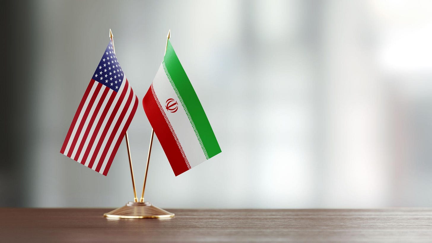 American And Iranian Flag Pair On A Desk Over Defocused Background