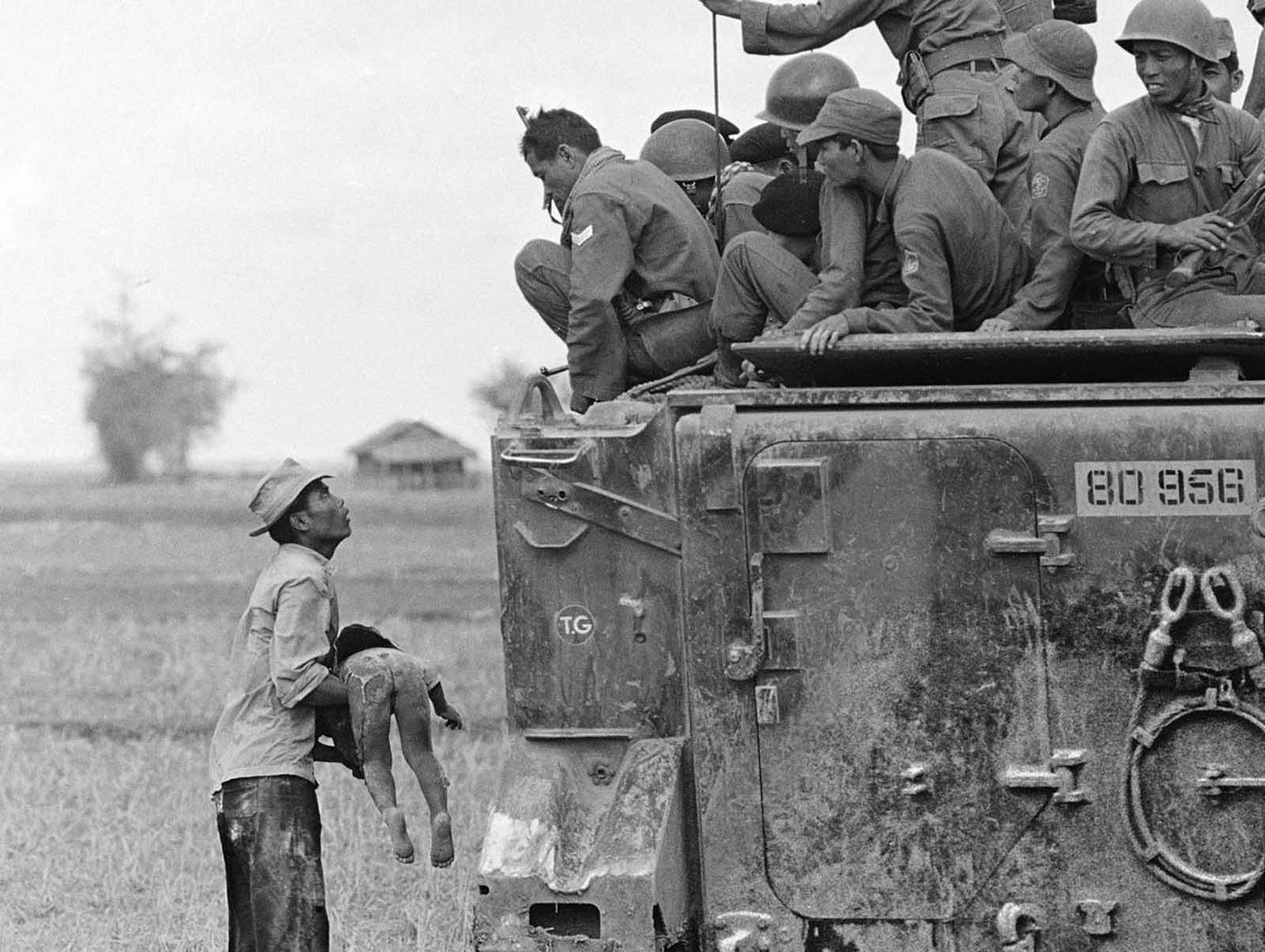 A distraught father cradles his deceased child, killed during a government forces' pursuit of guerrillas into a village near the Cambodian border, as South Vietnamese Army Rangers observe from their armored vehicle, March 19, 1964. A distraught father cradles his deceased child, killed during a government forces' pursuit of guerrillas into a village near the Cambodian border, as South Vietnamese Army Rangers observe from their armored vehicle, March 19, 1964.