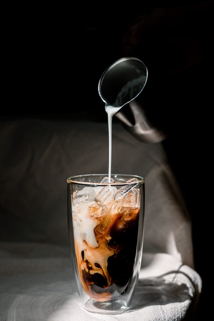 Pouring cream into a glass of iced coffee. Pouring cream into a glass of iced coffee.