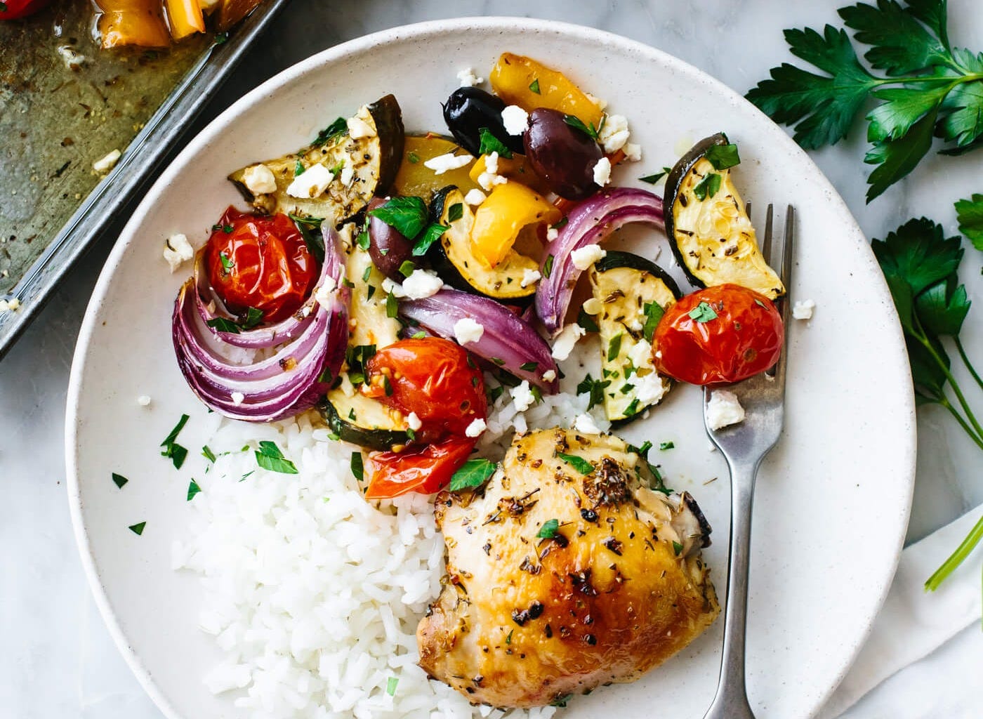 Greek sheet pan chicken plated with rice next to tongs. Greek sheet pan chicken plated with rice next to tongs.