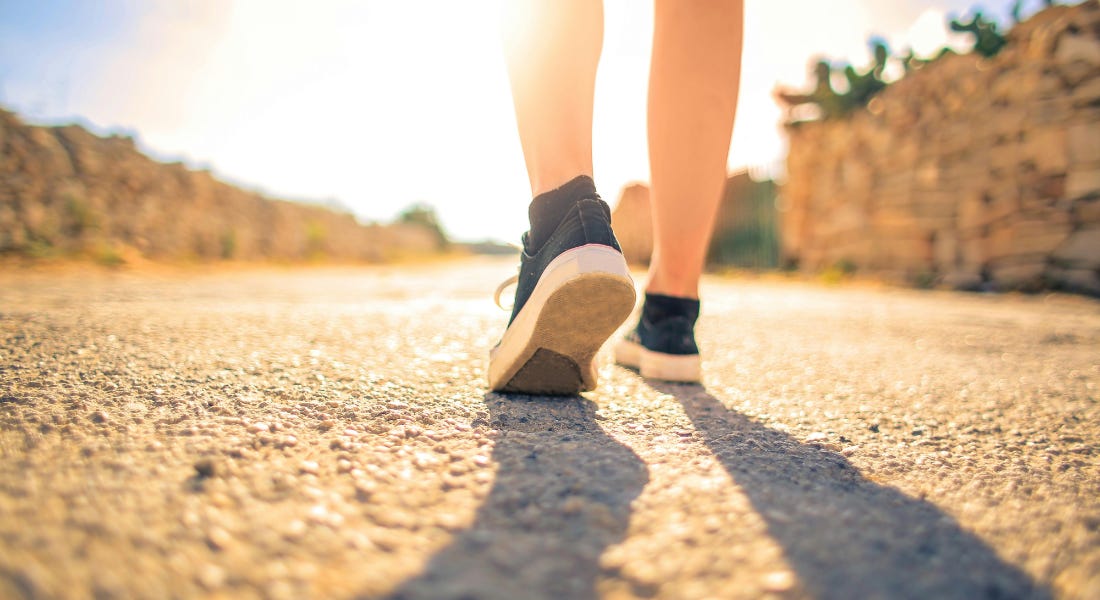 A person walking with navy blue trainers on a road, with the sky shining in front of them A person walking with navy blue trainers on a road, with the sky shining in front of them