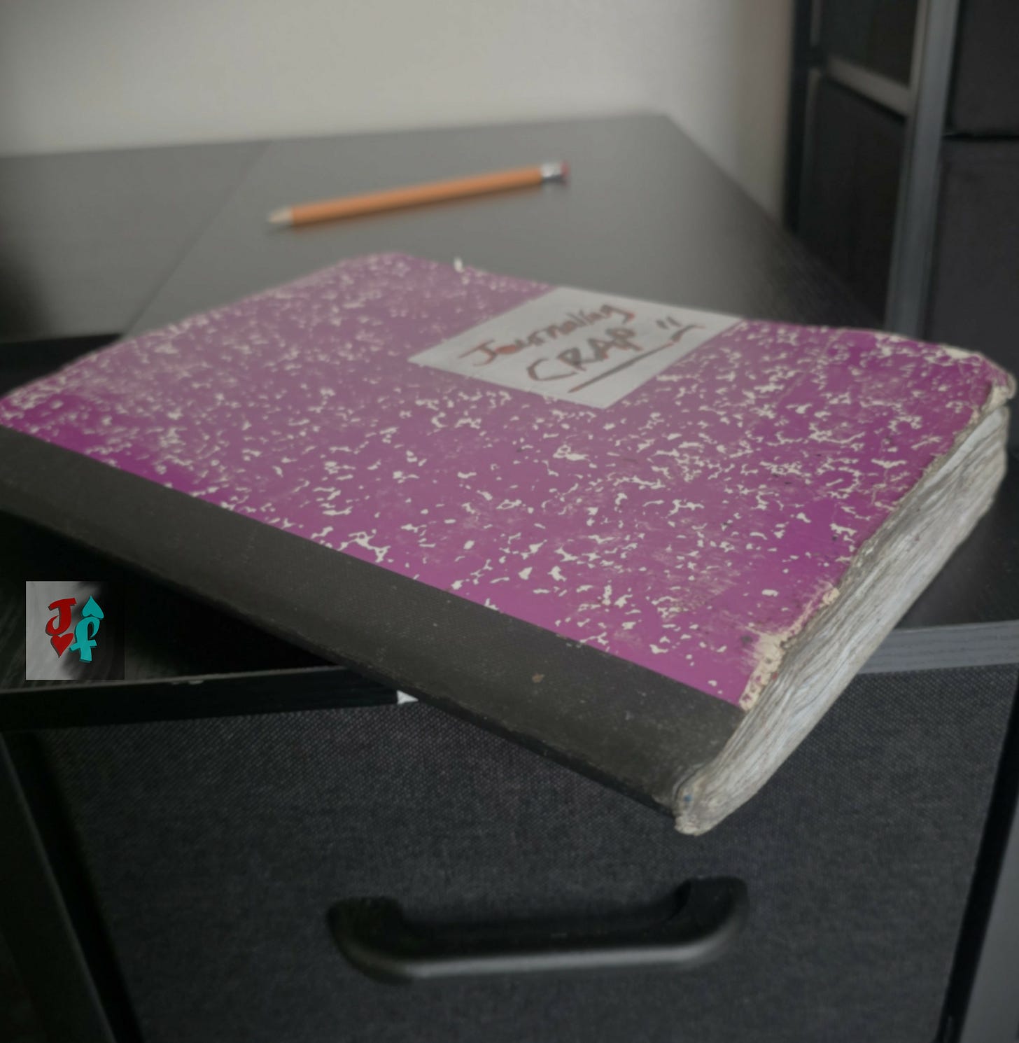 A photo of a dirty, purple notebook labelled, "Journaling Crap," sitting on a black desktop in a well-lit room.