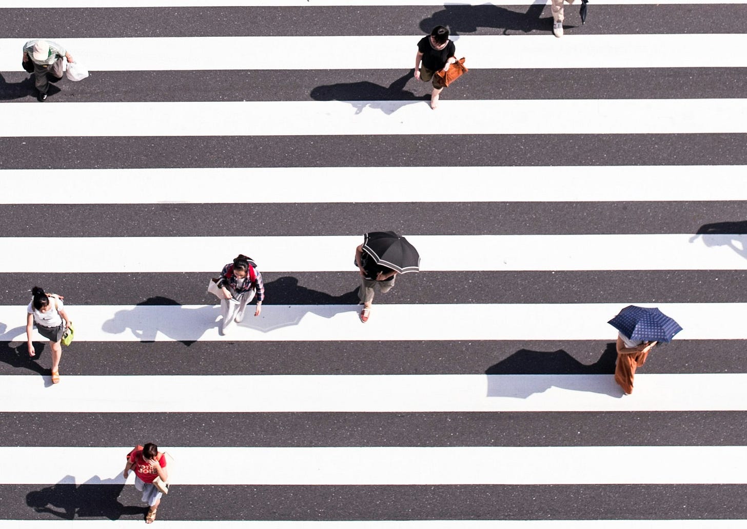 Aerial view of people crossing a crosswalk with white lines on a black road.