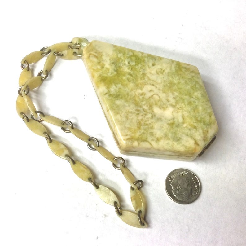 May include: A green and white marbled, rectangular shaped, hinged box with a gold chain. The chain is made of oval-shaped links. The box is about the size of a dime.