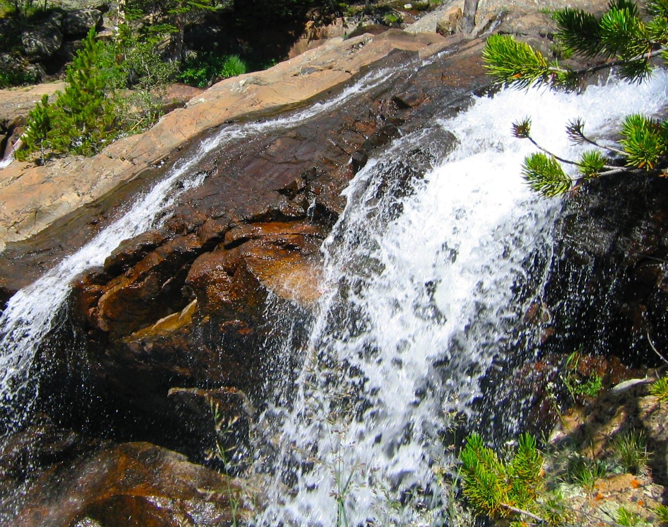 Water streaming down brown rocks under bright sun, a Rocky Mountain scene