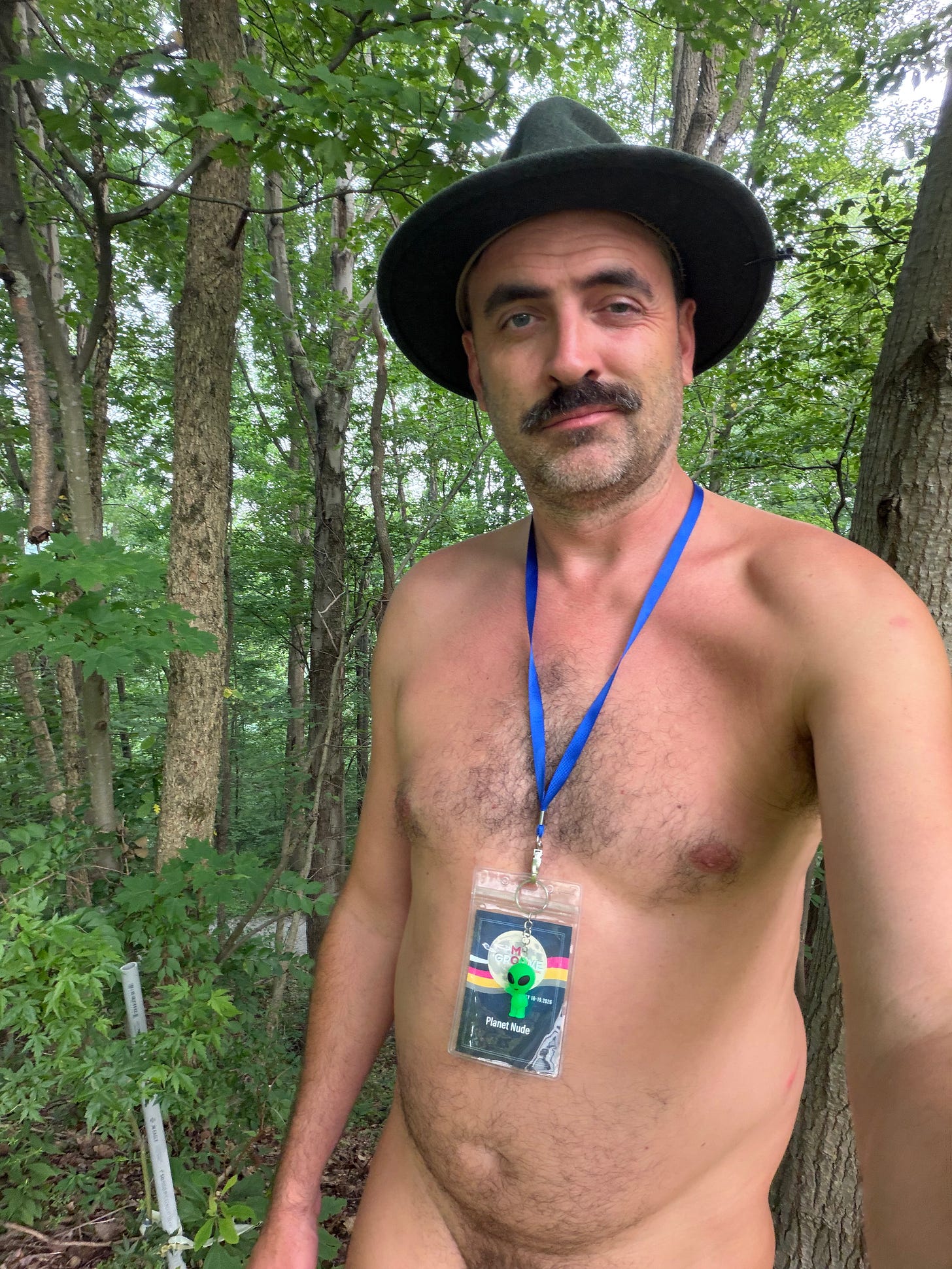 Evan Nix stands outdoors among trees, wearing a wide-brimmed hat and a blue lanyard with a MoonGroove and Planet Nude badge. Evan Nix stands outdoors among trees, wearing a wide-brimmed hat and a blue lanyard with a MoonGroove and Planet Nude badge.