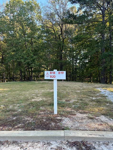 a road with trees, sign for tent sites B18, B19, B20, 3 motorcycles parked in the gravel near the tent sign