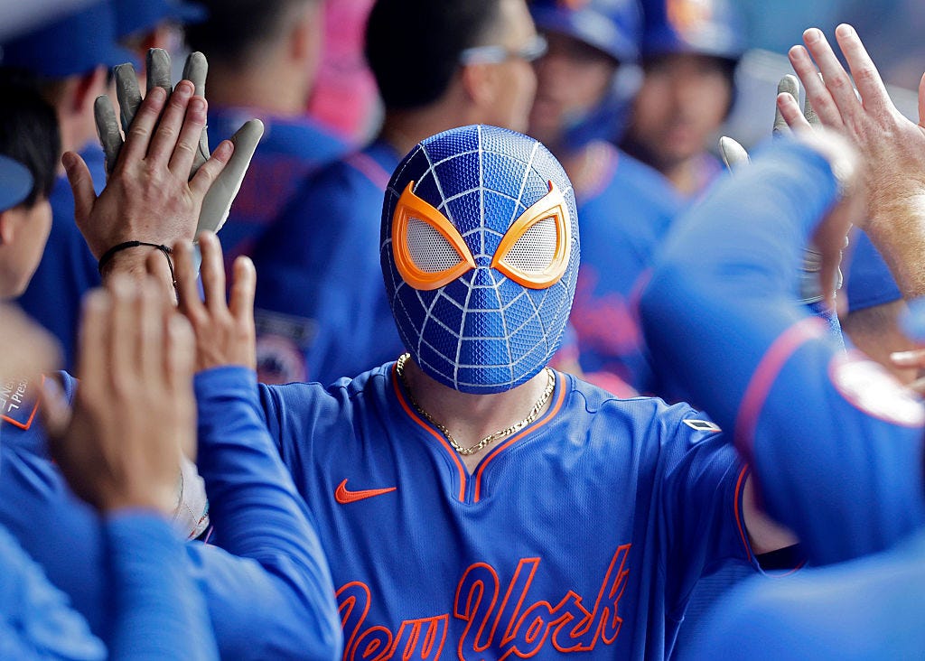 AJ Ewing walks through the dugout hi-fiving teammates wearing a Mets-themed Spiderman mask.