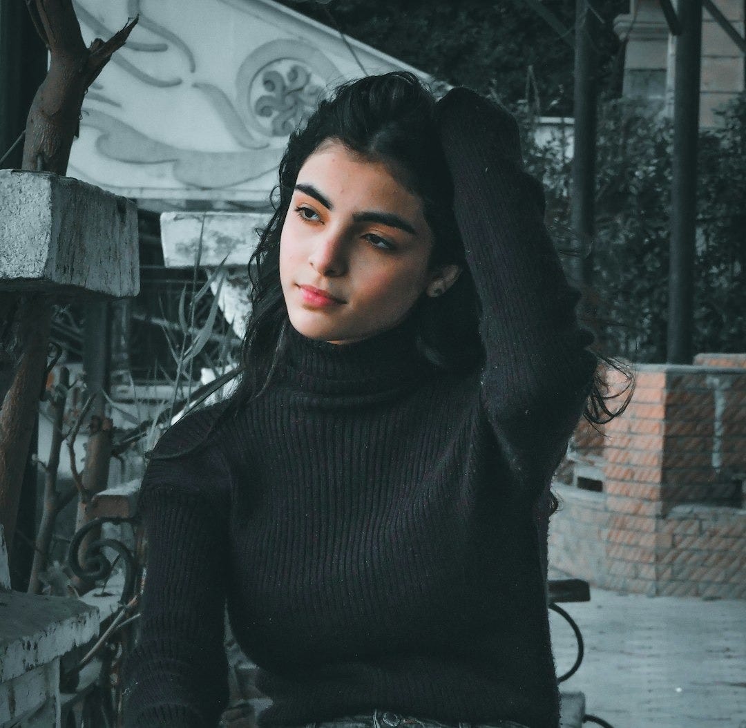 woman in black turtleneck sweater and blue denim jeans sitting on black metal fence