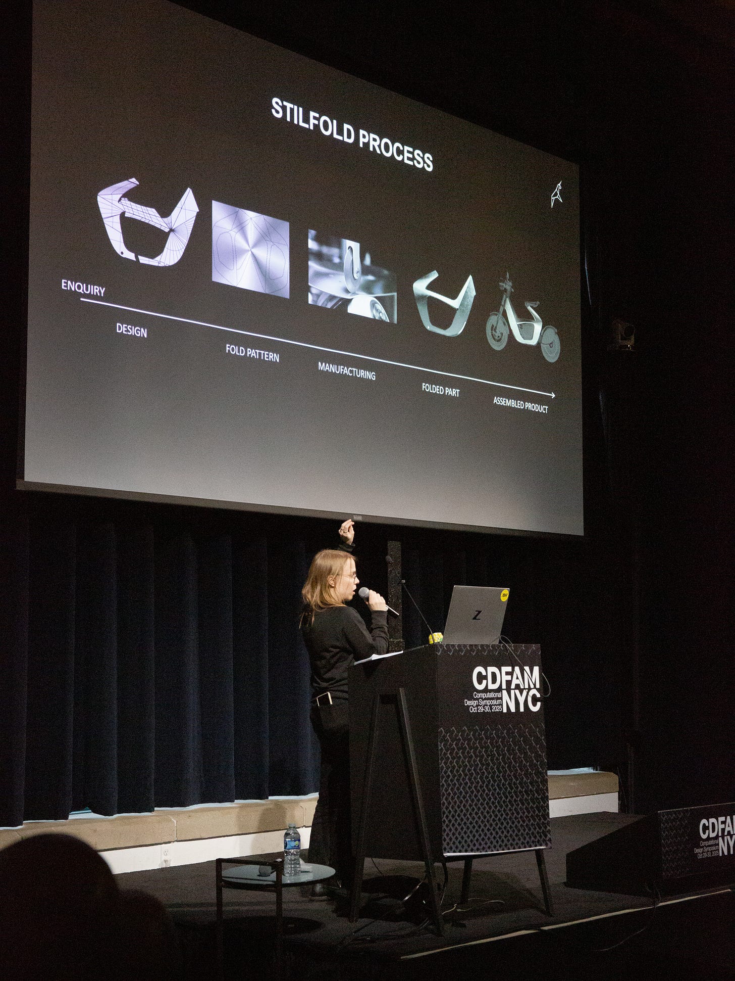 A speaker presenting the 'Stilfold Process' during a computational design conference, showcasing various stages from inquiry to the assembled product on a large screen.