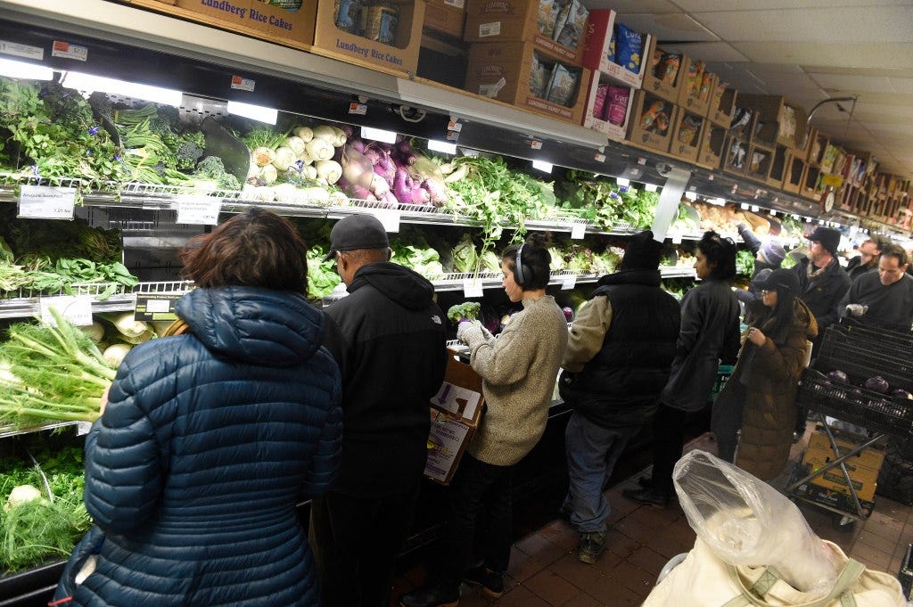 Shoppers selecting fresh produce from a brightly lit display at the Park Slope Food Coop in Brooklyn, New York.