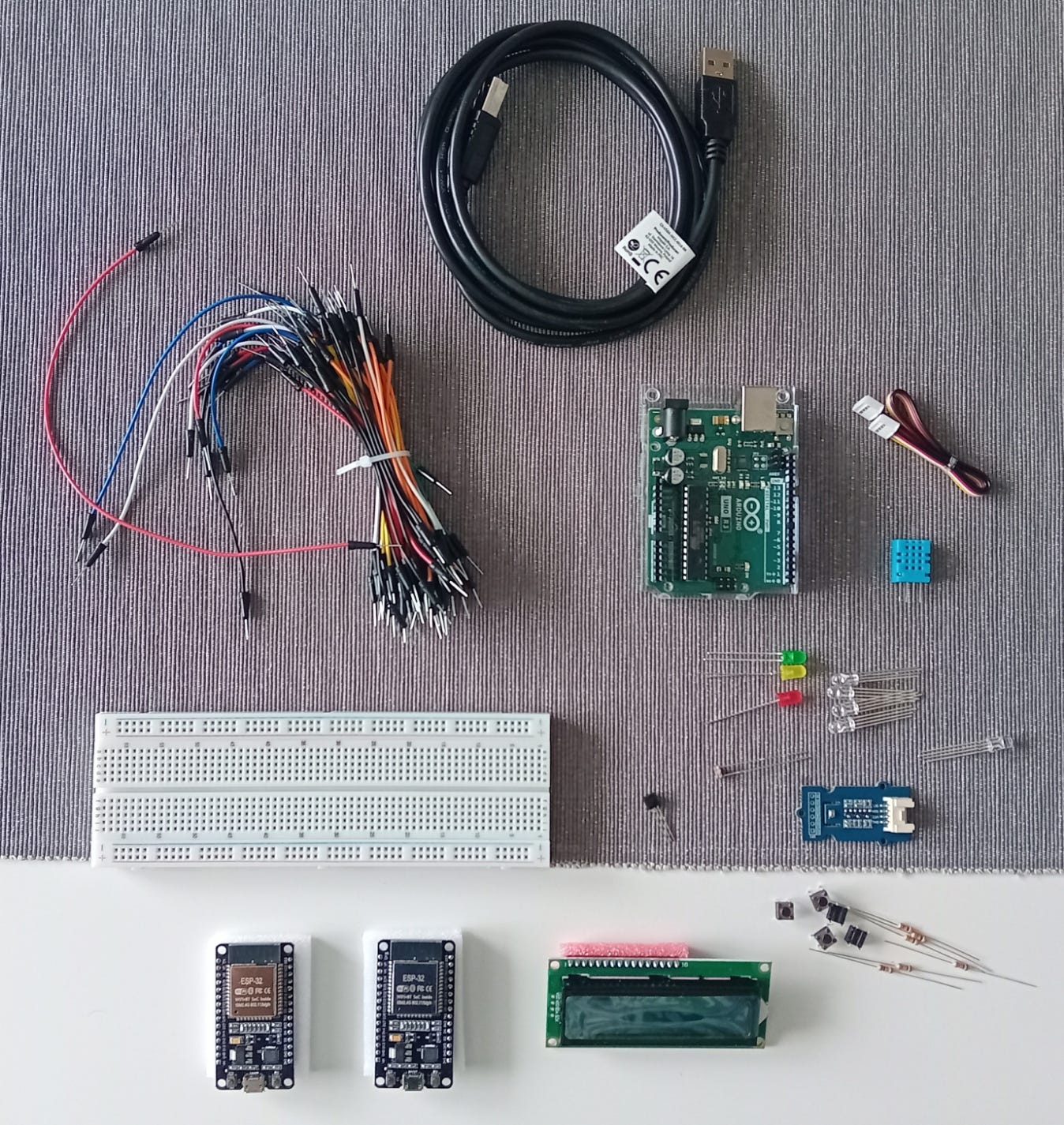 Na zdjęciu widać różne urządzenia elektroniczne i przewody. Między innymi: Arduino Uno Rev3, dwie płytki ESP DevKitC, mały wyświetlacz LCD, białą płytkę stykową, przewody połączeniowe do płytki stykowej, diody LED, rezystory, przełączniki tact switch, czujniki temperatury i ciśnienia. Na zdjęciu widać różne urządzenia elektroniczne i przewody. Między innymi: Arduino Uno Rev3, dwie płytki ESP DevKitC, mały wyświetlacz LCD, białą płytkę stykową, przewody połączeniowe do płytki stykowej, diody LED, rezystory, przełączniki tact switch, czujniki temperatury i ciśnienia.