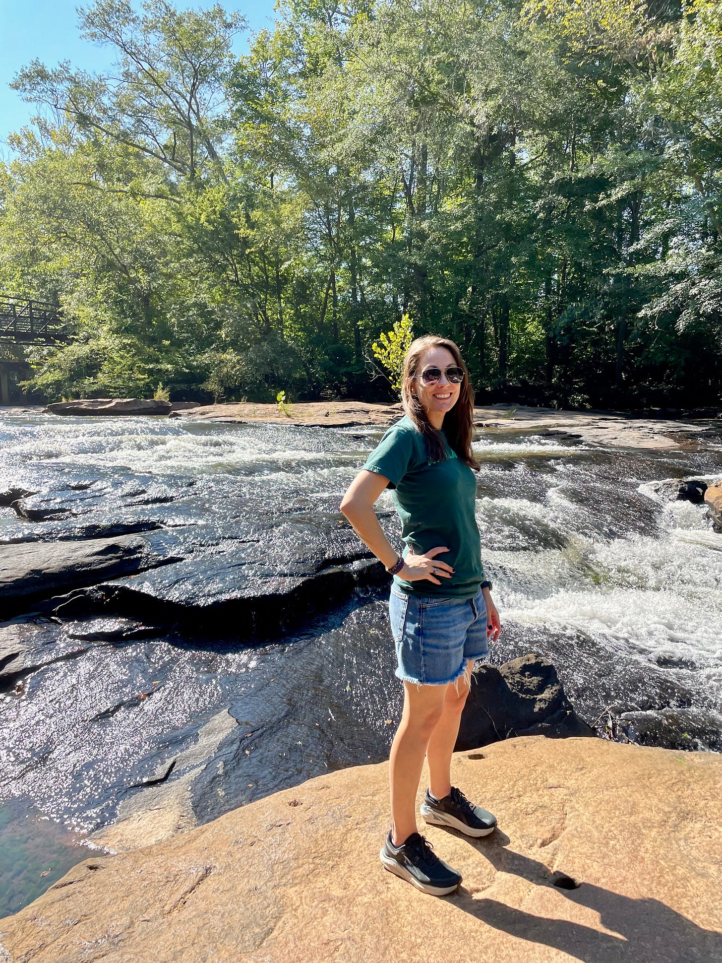 a photo of Kendra standing on a rock in the middle of a creek. She is smiling at the camera.