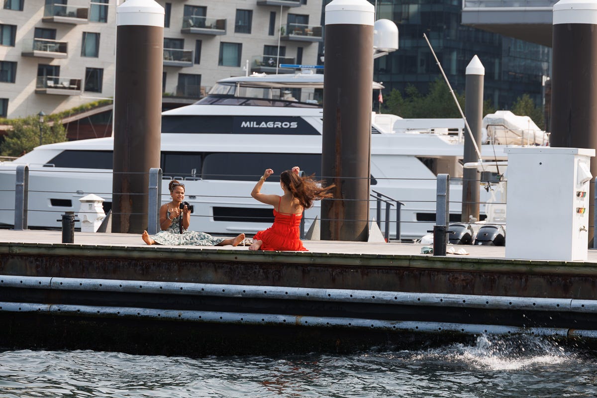 Woman in red dress posing for a photographer on a dock in Boston Harbor with a large yacht in background
