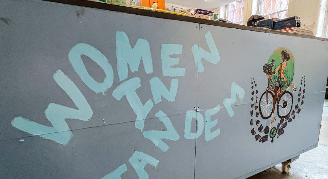 A blue sign that says 'women in tandem' on it, with an illustration of a woman on a bike to the right of it A blue sign that says 'women in tandem' on it, with an illustration of a woman on a bike to the right of it
