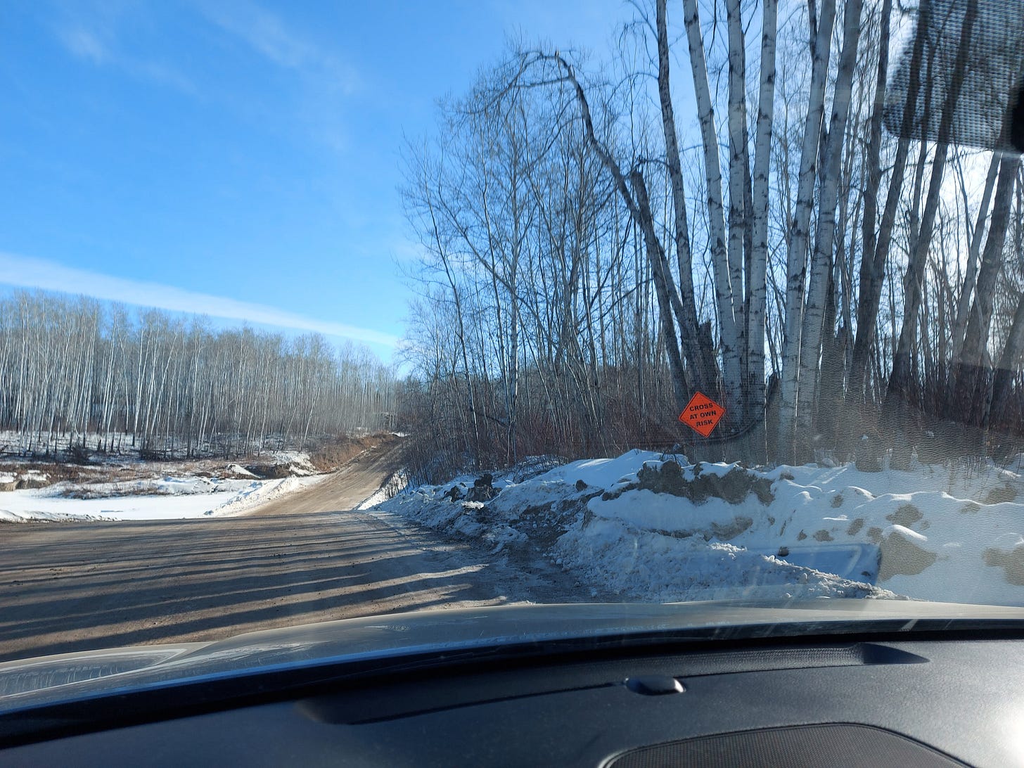 photo from a windshield on an ice road with a cross at your own risk sign