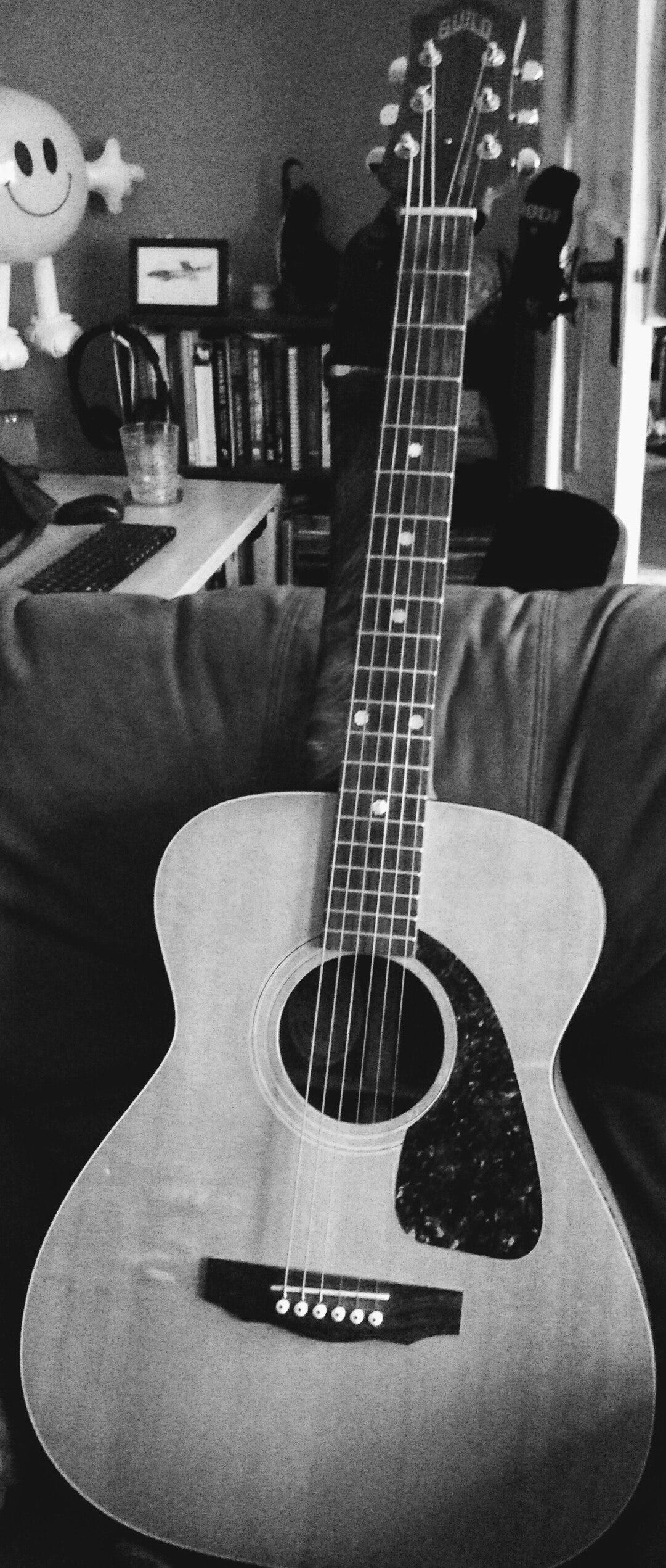 A black and white image of a Guild acoustic guitar propped in an armchair. 