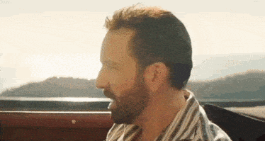 a man with a beard is sitting in the back seat of a car looking out the window .