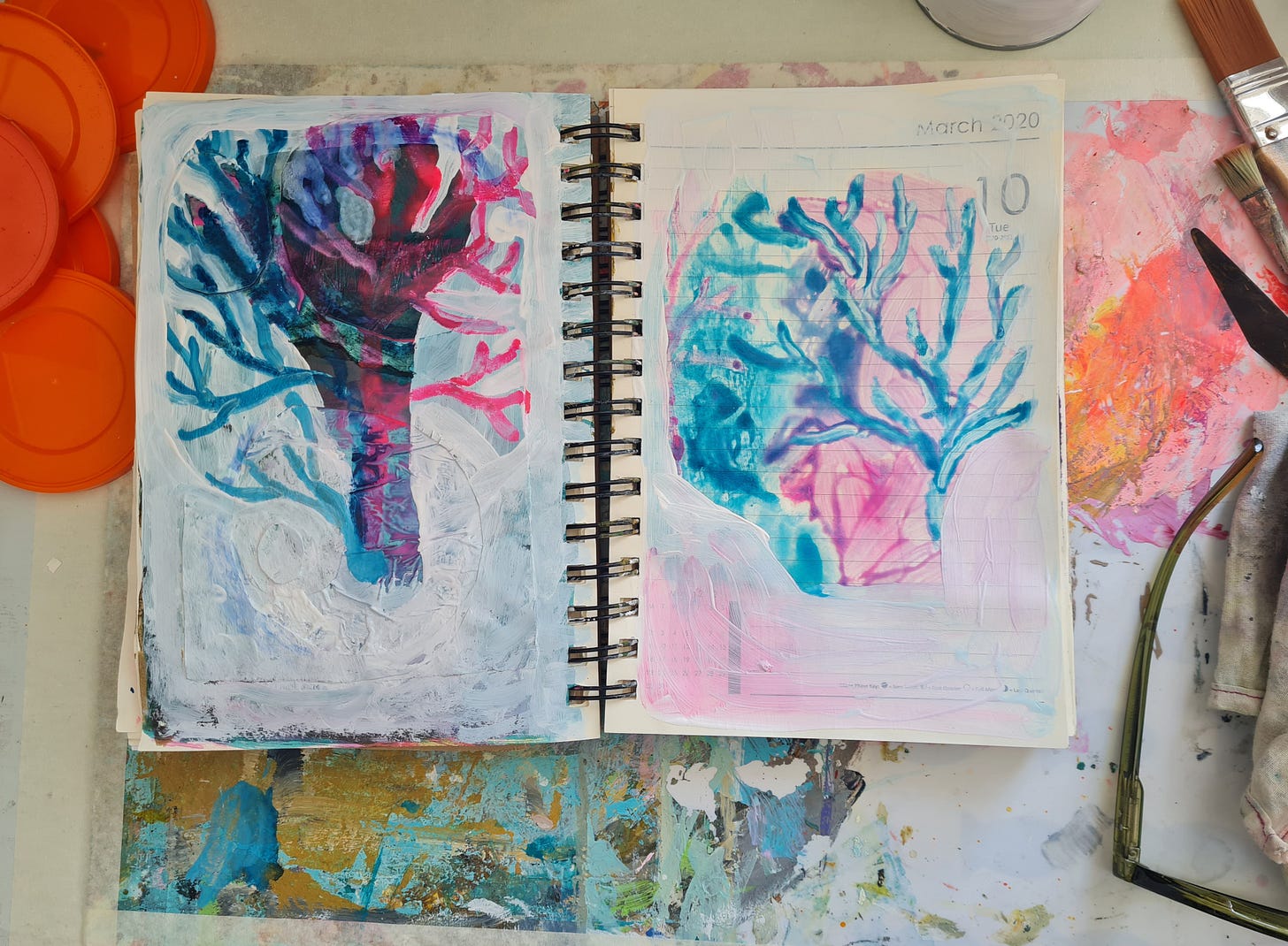 An open sketchbook lying on a desk. The pages have ink sketches that look like trees in blue and pink colours.