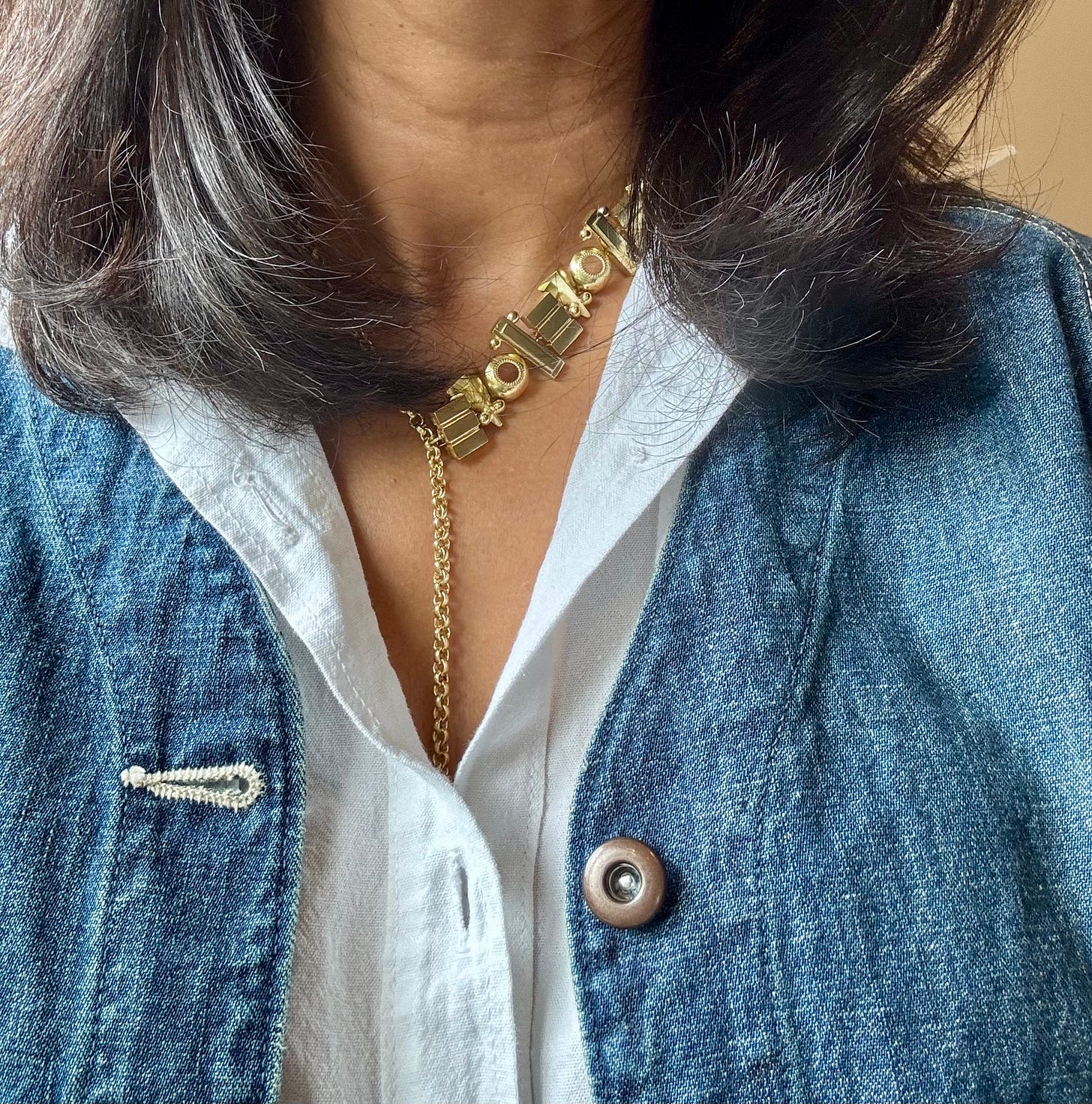 Close-up of Surmeyi Love Lariat necklace in brass layered over a white Oaxacan guayabera and a blue Chimala work jacket.