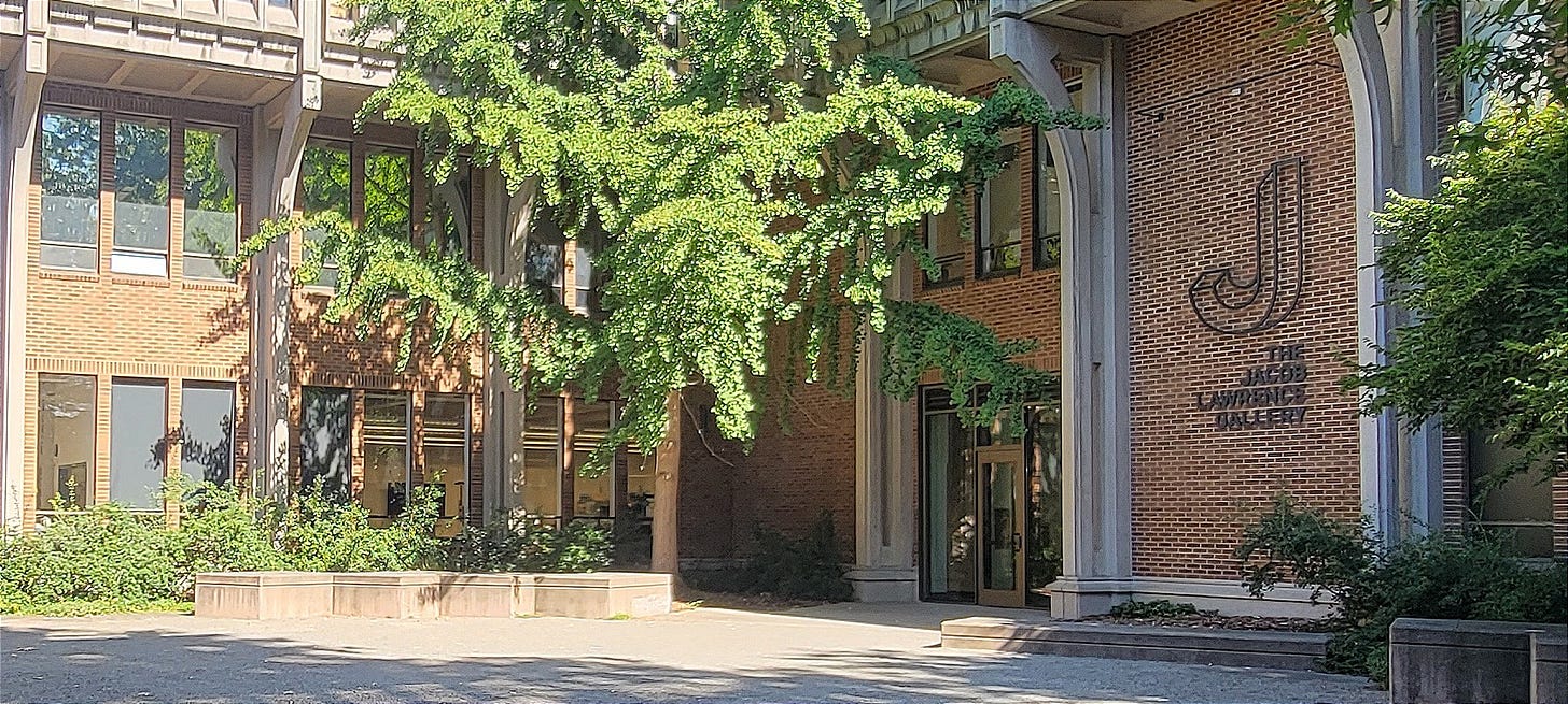 Sunny open gravel courtyard in front of the the Jacob Lawrence Gallery with surrounding trees and foilage.
