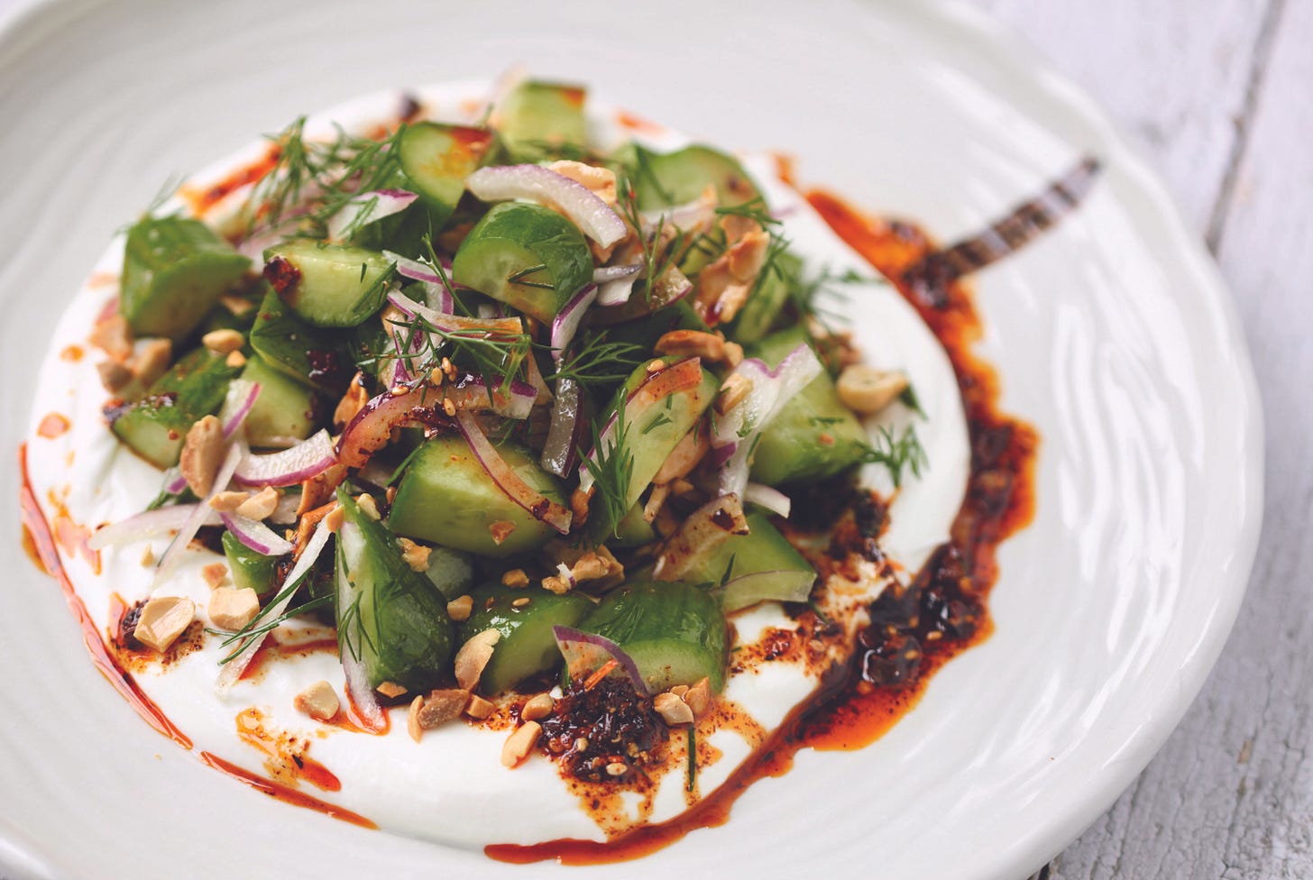 wide-brimmed plate with yogurt and cucumber salad with chile oil.