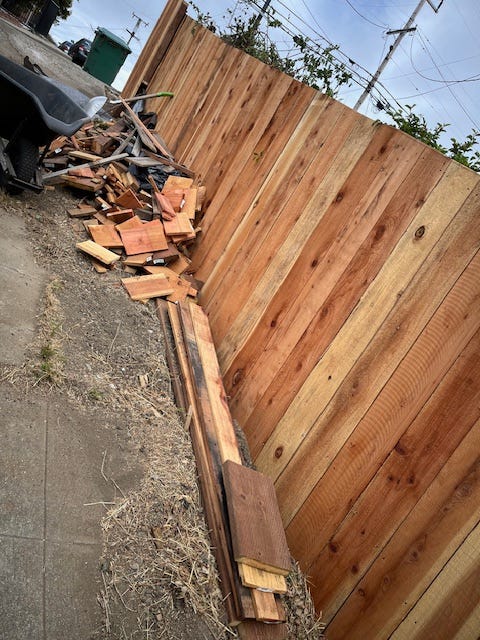 Piece of a new redwood fence with a big pile of wood scraps piled up against it.