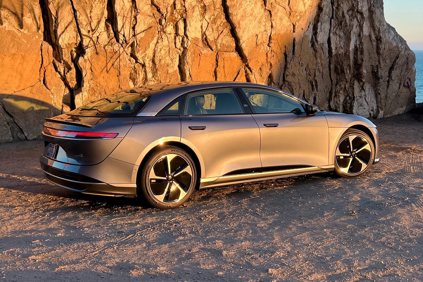 Rear quarter view of a 2023 Lucid Air at sunset, parked next to a rock wall.