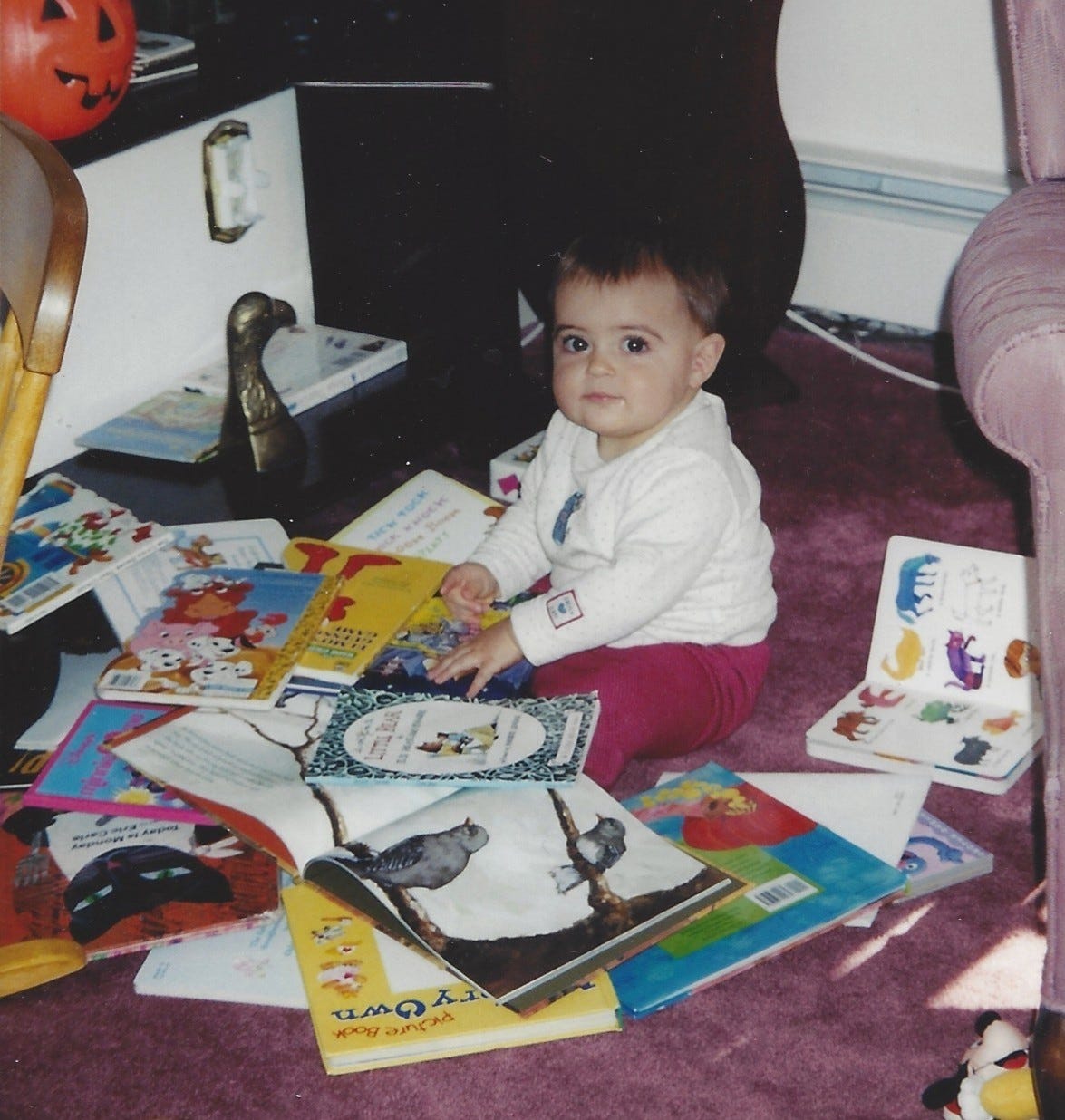 10-month-old baby girl sitting of the floor surrounded by two dozen picture books she's pulled off a bookshelf