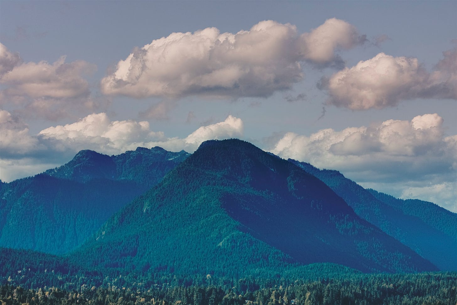 A mountin covered in evergreen trees rises up to touch the sky. Exhale, it feels just like otium.