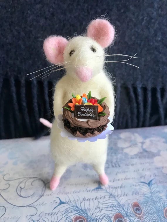 A felt mouse figurine holding a birthday cake. A felt mouse figurine holding a birthday cake.