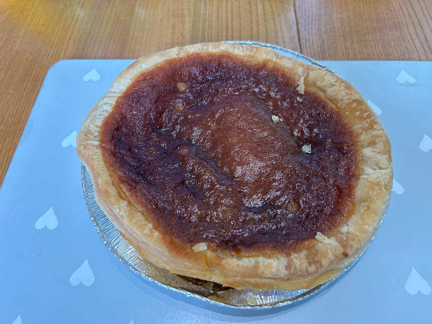 A Bakewell Pudding sat in its foil container on a table. A Bakewell Pudding sat in its foil container on a table.